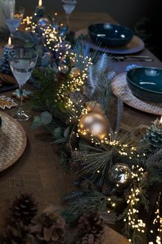 the table is set with pine cones, evergreen branches and other holiday decorating items