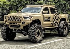 a tan truck is parked in a parking lot with trees behind it and bushes on the other side