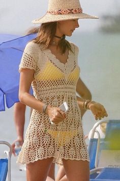 a woman walking on the beach in a yellow crochet dress and straw hat