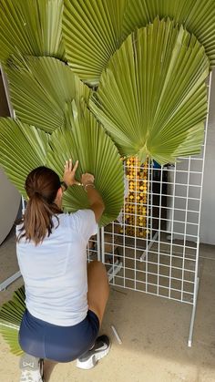 a woman is sitting on the ground working on a large green palm fronde