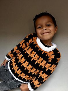 a little boy sitting on the floor wearing a black and orange crochet sweater