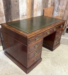 an old wooden desk with leather top and two chairs in front of a wood wall