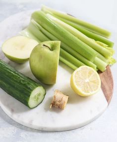 an apple, cucumber, lemon and celery on a marble plate