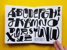 a hand holding up an open book with black letters on it and the words alphabet written in