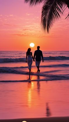 a couple walking on the beach at sunset