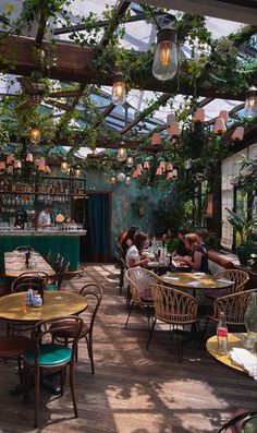 people are sitting at tables in an outdoor dining area with plants growing on the ceiling