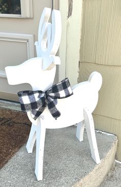 a white rocking horse with a black bow on it's head sitting in front of a door