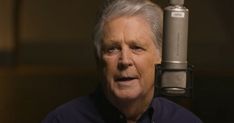 an older man with grey hair is sitting in front of a microphone and looking at the camera