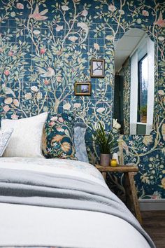 a bed sitting under a window next to a wallpaper covered in flowers and birds