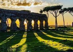 the sun is setting behind an old stone structure with arches and trees in front of it