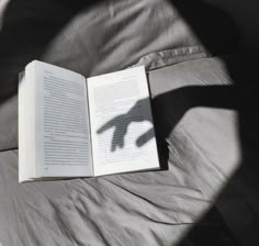 an open book sitting on top of a bed next to a hand casting a shadow