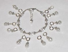 a silver bracelet with white pearls and charms on it's side, sitting on a white surface