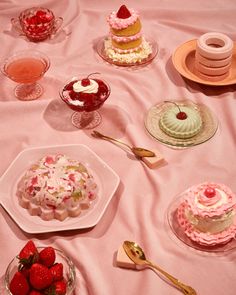 a table topped with cakes and desserts on top of a pink cloth covered table