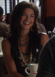 a woman sitting at a table with a coffee cup in front of her and smiling