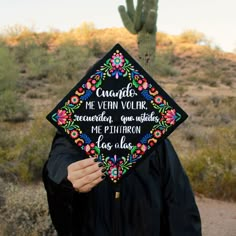 a person wearing a graduation cap with embroidered words on it and a cactus in the background