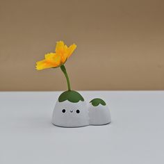 a yellow flower in a white vase with two small rocks on the table next to it