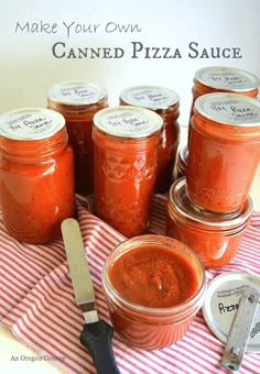 several jars of canned pizza sauce sitting on a table with a knife and spoon next to them