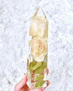 a person holding a clear vase with flowers in it on a white surface, while the image is being taken from above