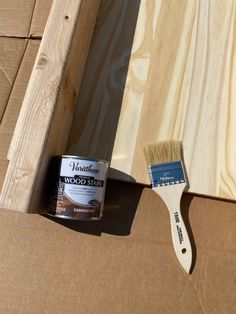 a paint can and brush sitting on top of a piece of wood