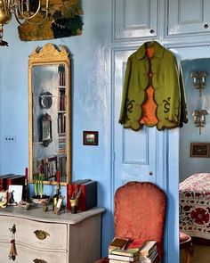 a bedroom with blue walls and an old fashioned chair in front of a mirror on the wall