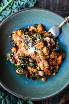 a blue bowl filled with pasta and spinach covered in sauce on top of a wooden table