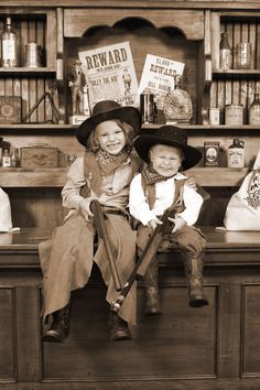 two young children sitting on top of a wooden counter in front of bookshelves