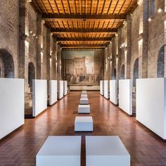 an empty room with benches and paintings on the wall behind it, in front of a brick ceiling