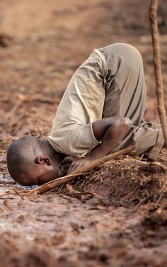 a young boy is laying down in the mud with his head resting on a stick