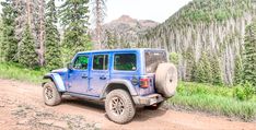 a blue jeep driving down a dirt road next to trees and grass on a hillside