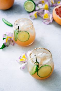 two glasses filled with drinks and garnished with cucumbers, lemons, and grapefruit