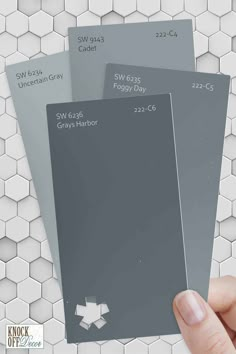 three shades of gray paint being held up by a person's hand in front of hexagonal tiles