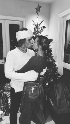 black and white photograph of two people kissing in front of a christmas tree with presents on the floor