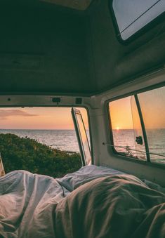 the sun is setting over the ocean from inside a vehicle with two windows and a bed in it