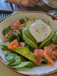 a salad with salmon, avocado and sour cream in a bowl on a table