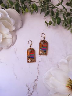 two colorful earrings sitting on top of a marble surface next to flowers and leaves,