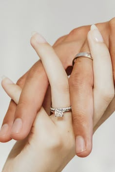 two hands holding each other with their wedding rings on top of one another's fingers