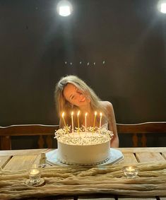 a woman sitting in front of a white cake with lit candles on top of it