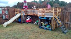 an outdoor play area with a slide and wooden pallets in the back yard, next to a fence