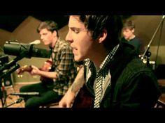 two young men sitting in front of microphones playing guitars and singing into a mic