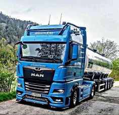 a large blue truck parked on the side of a road next to a lush green hillside