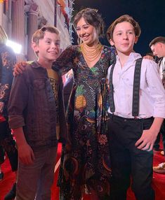 two boys and a woman standing on a red carpet