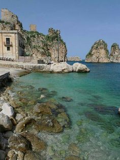 the water is crystal blue and clear with rocks in front of it, along with an old building