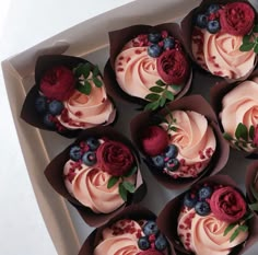 twelve cupcakes with pink frosting and berries on top in a white box