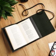 an open book sitting on top of a wooden table next to a pair of glasses