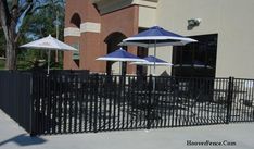 several umbrellas are set up on the side of a fenced in area with tables and chairs