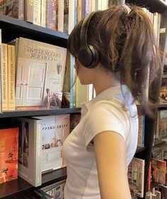 a woman wearing headphones looking at books on a book shelf in a bookstore or library