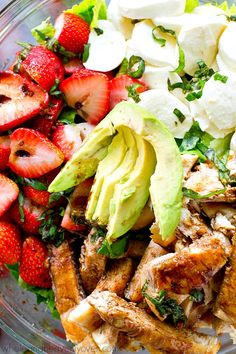 a bowl filled with chicken, avocado, strawberries and other foodstuffs