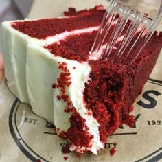 a piece of red velvet cake with white frosting being held up by a fork