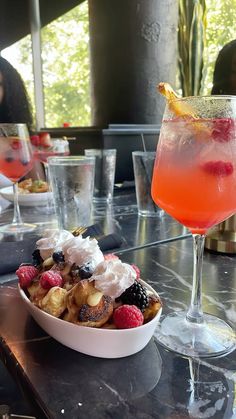 a bowl of fruit sits on a table next to a drink