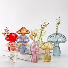 several different colored glass vases sitting on top of a white book with dried flowers in them